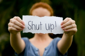 Woman holding piece of paper that reads, "Shut up!"
