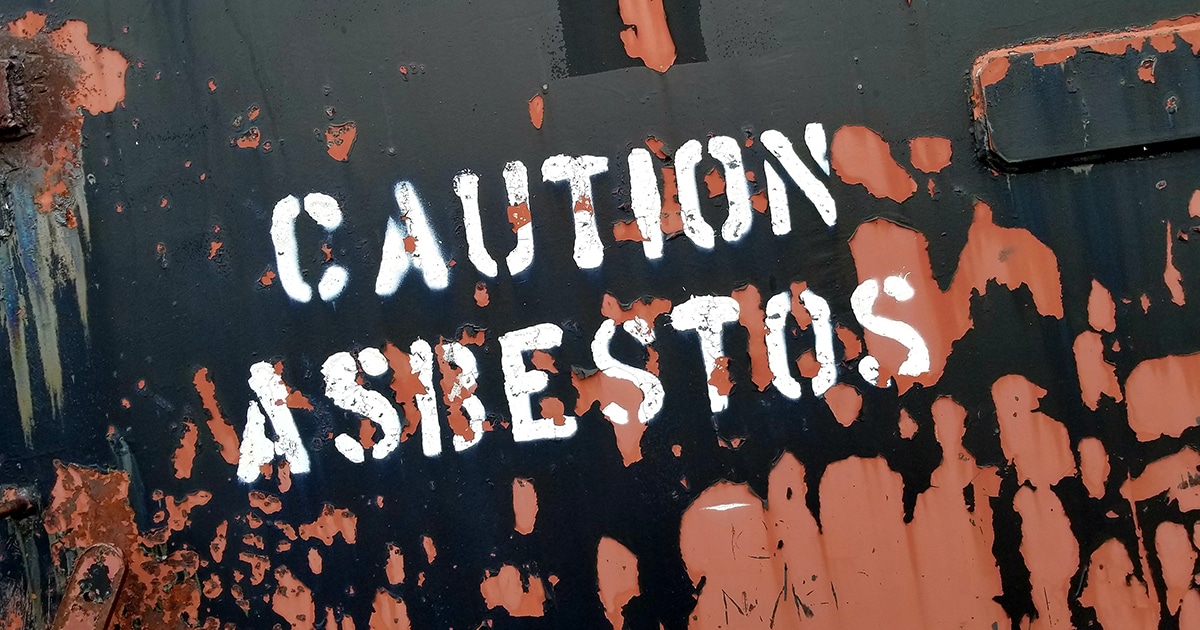 Caution Asbestos sign on rusting container